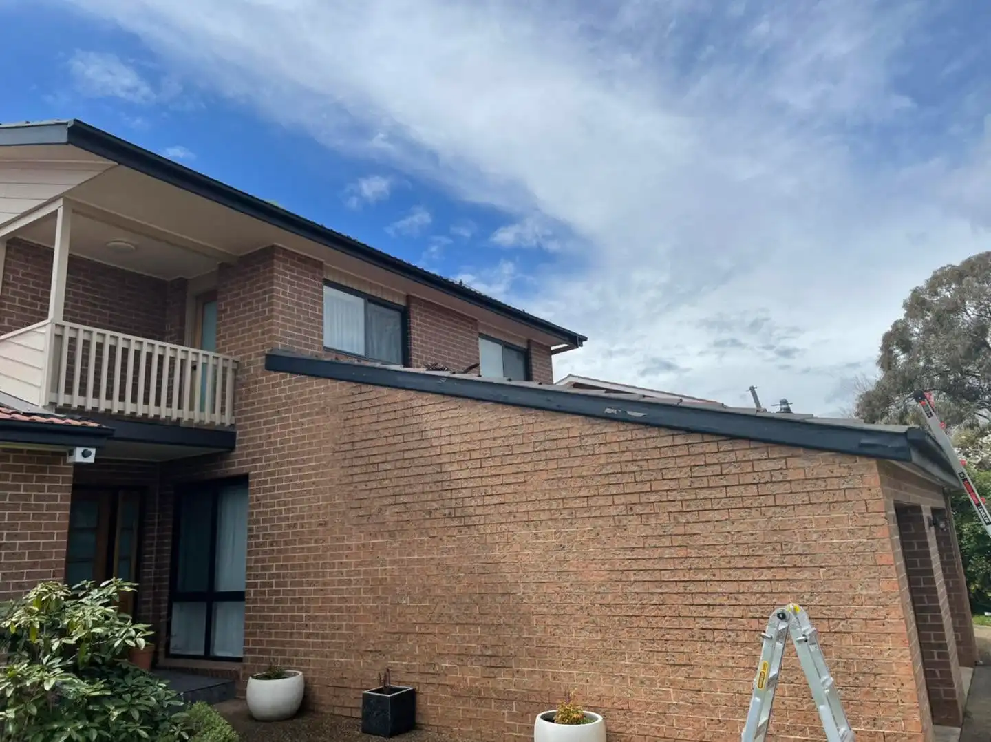 Side view with ladder showing new dark fascia, guttering and roof trim on the Canberra home