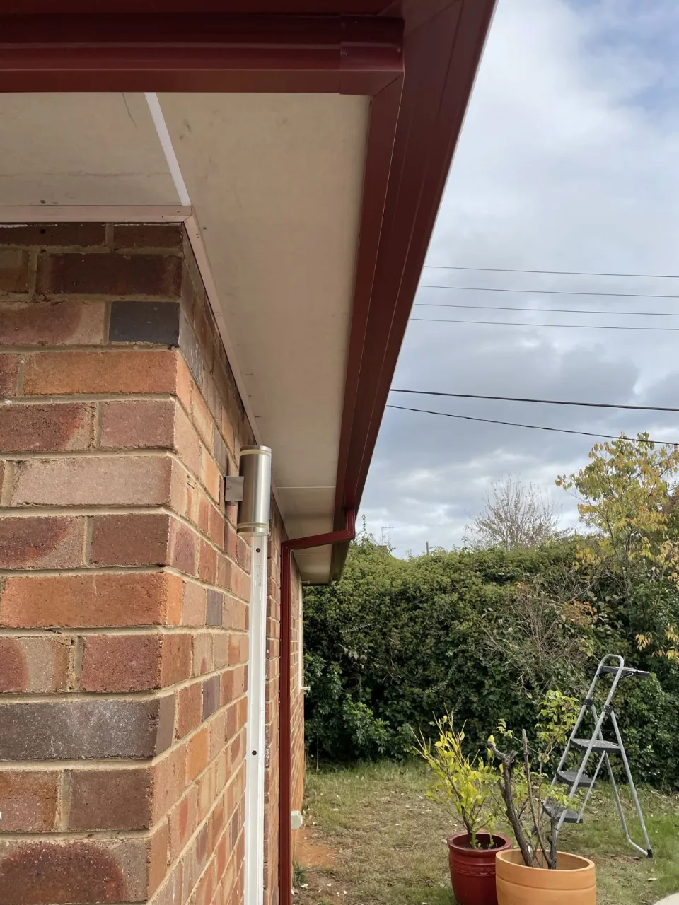 Close-up of new red fascia cover, guttering and eave sheeting with white downpipe